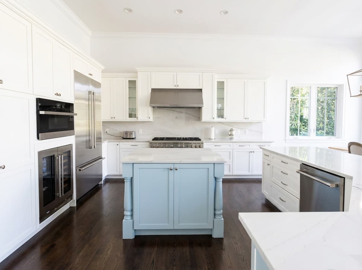 Bright coastal kitchen with blue island, white cabinets, marble counters, and family photos