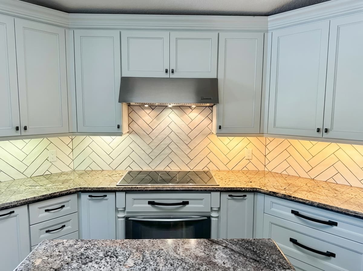 Refreshed kitchen with herringbone marble backsplash, white cabinets, and warm granite counters